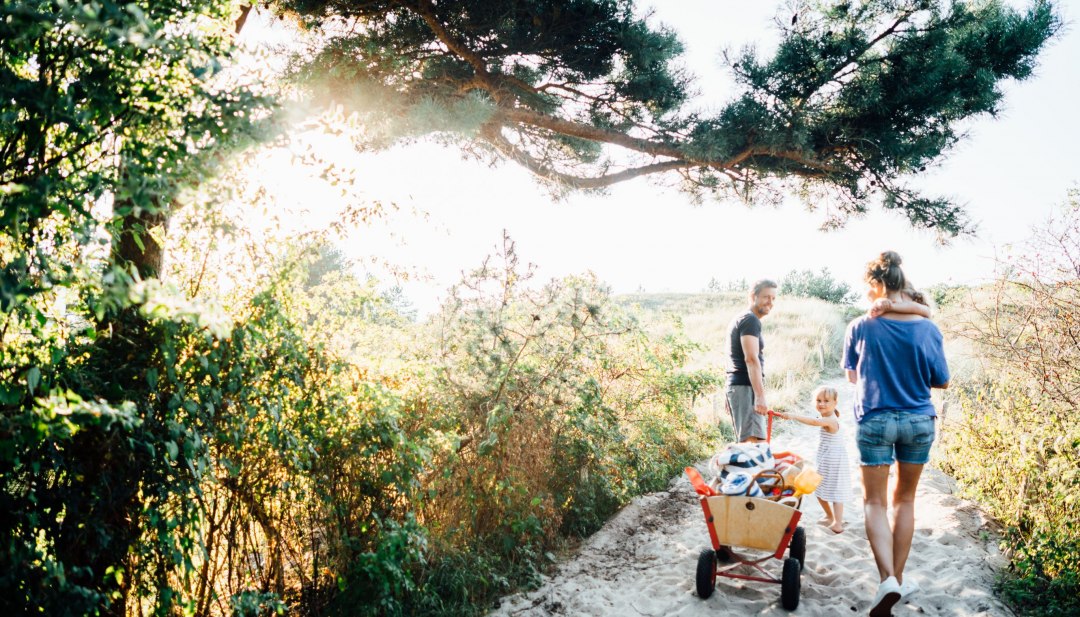 A family pulls a handcart with beach utensils barefoot towards the Baltic Sea beach in Dierhagen.