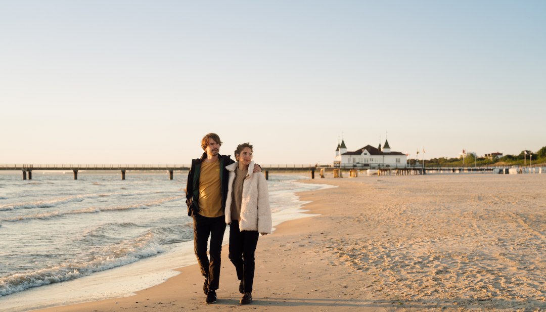 Paar aan het wandelen op het strand van Ahlbeck bij zonsopgang met pier op de achtergrond.