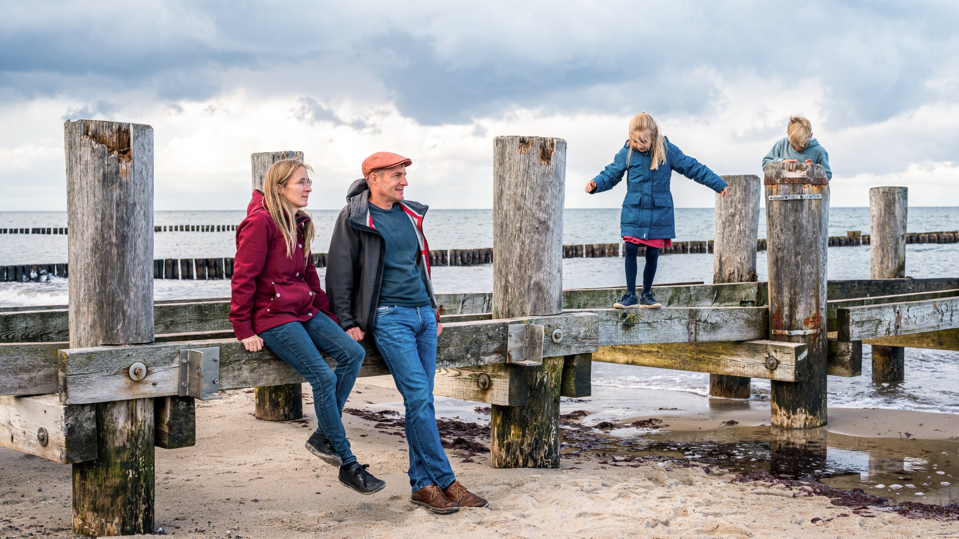 Outdoors in all weathers: family vacation at the Baltic Sea - here in Kühlungsborn, © TMV/Tiemann Family at an old wooden scaffolding for a pier on the beach in Kühlungsborn - the children are doing gymnastics on it.