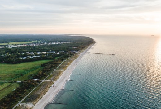 Aerial view of the pier and the beach of Graal-Müritz, surrounded by woods and meadows, with the Baltic Sea in the light of an atmospheric sunset.