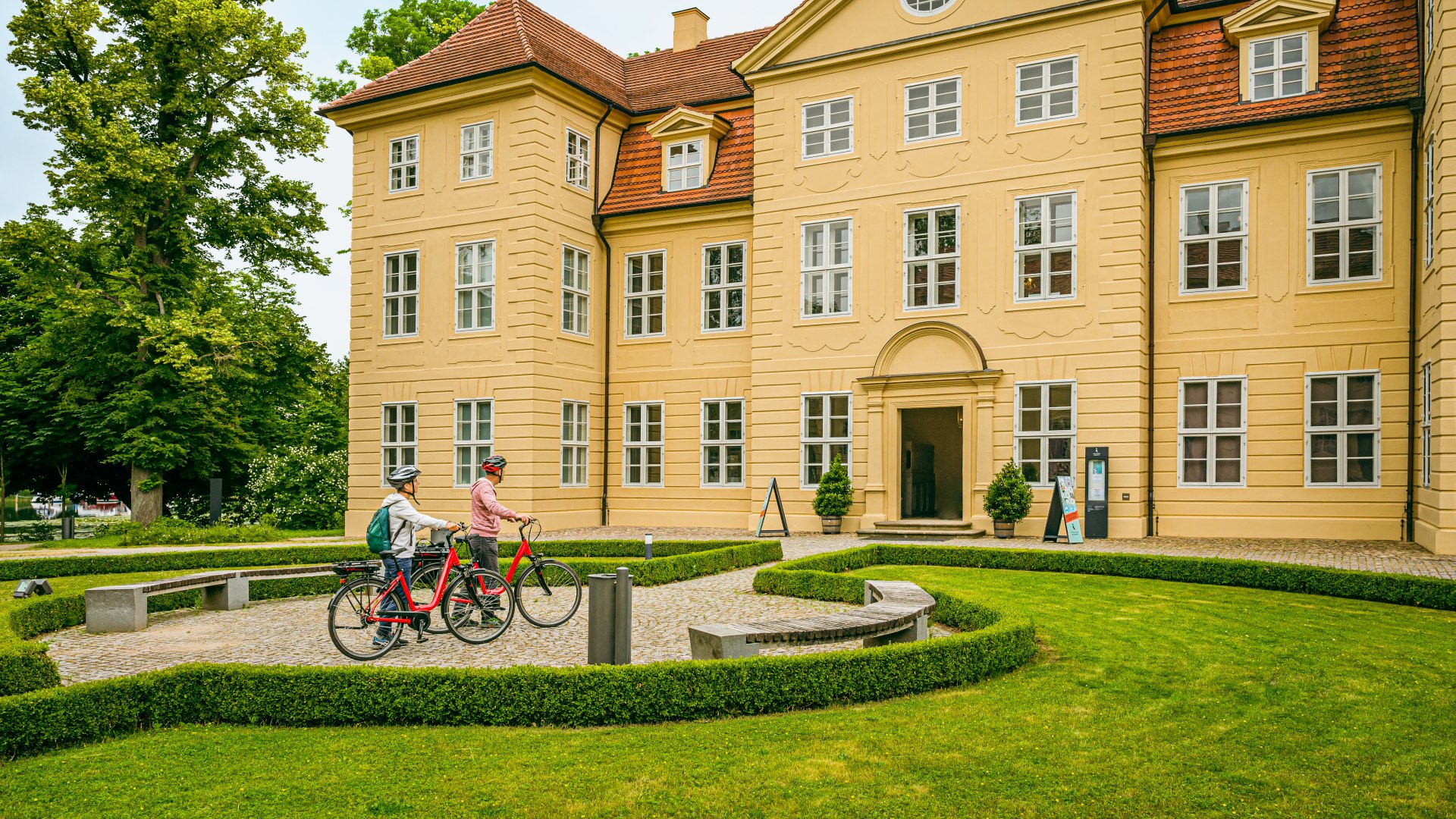 A couple with e-bikes stand in front of Mirow Castle