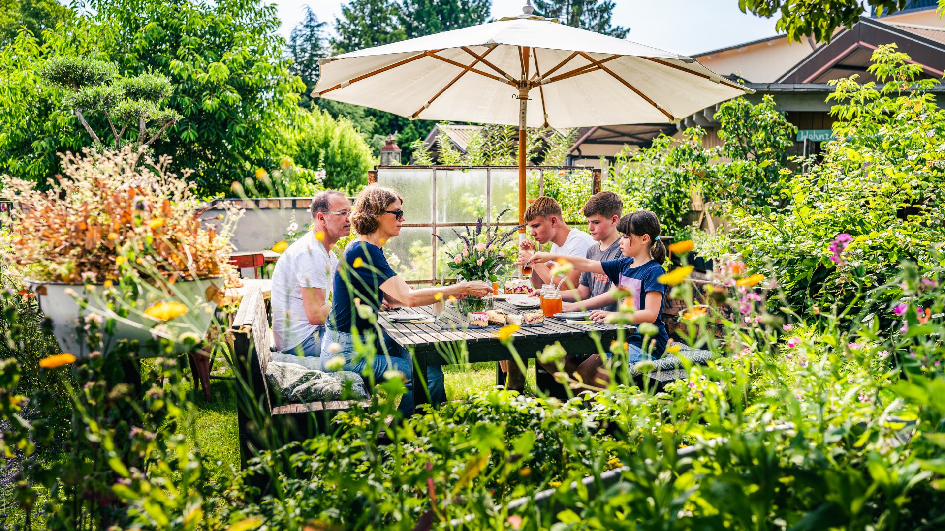 A family takes a coffee break in the café's garden, which is overgrown with plants.