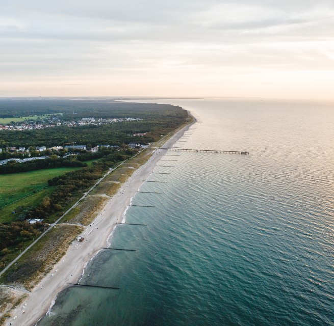 Luchtfoto van de pier en het strand van Graal-Müritz, omgeven door bossen en weilanden, met de Baltische Zee in het licht van een sfeervolle zonsondergang.