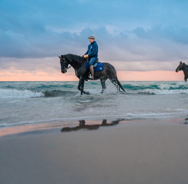 Twee ruiters te paard gaan strandrijden bij zonsondergang aan de Oostzee op het schiereiland Fischland-Darß-Zingst