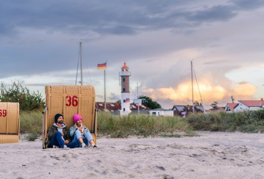 Couple sitting in a beach chair on the beach in Timmendorf on Poel with a view of the lighthouse and the evening sky.