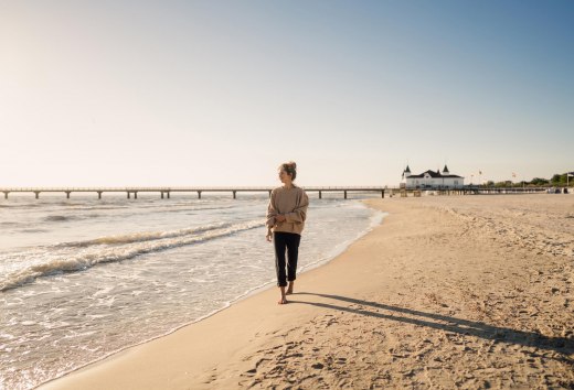 Kobieta spacerująca po plaży Ahlbeck o wschodzie słońca z molo w tle