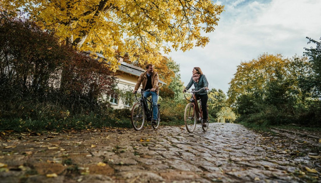Twee mensen fietsen op kasseien in de buurt van het landgoed Pohnstorf in de herfst.