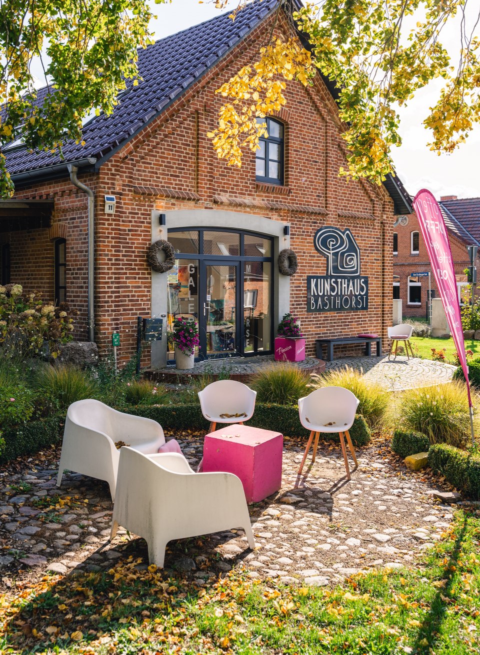 The Kunsthaus Basthorst in an autumnal garden, surrounded by yellow and green leaves, with outdoor seating.