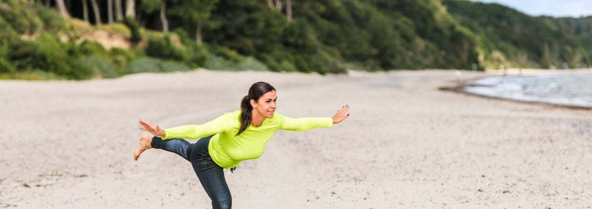 Een vrouw doet de &quot;staande balans&quot; op het strand en houdt haar evenwicht.