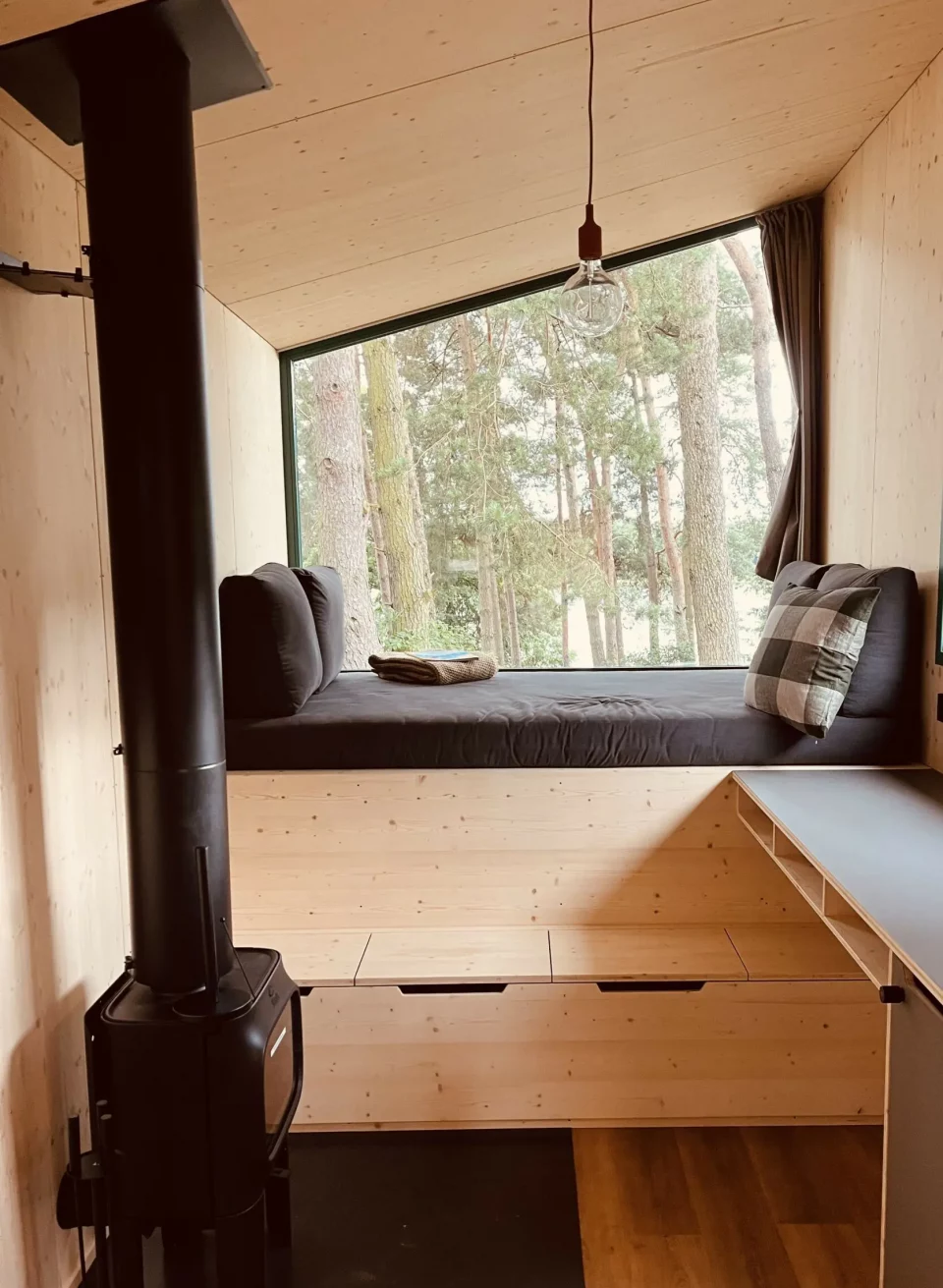 Minimalistisch wonen, maximale ontspanning - stijlvolle houten tiny houses bieden natuurlijk comfort voor een speciale time-out., © Ahoi Camp Canow Gezellig interieur van een klein huisje met houten lambrisering, houtkachel en een groot panoramisch raam met uitzicht op het bos.