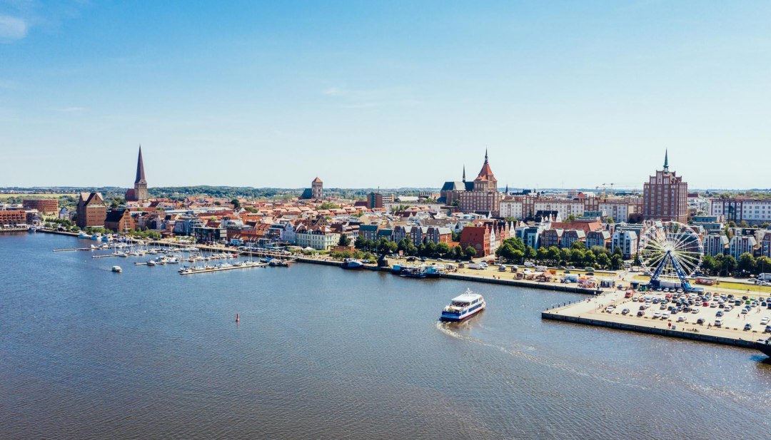 Van bovenaf ziet de stadshaven van Rostock eruit als een miniatuurwonderland. Zelfs het reuzenrad lijkt opeens niet meer zo groot. De excursieboot vaart rustig naar de steiger om nieuwe passagiers op te pikken., © TMV/Gänsicke