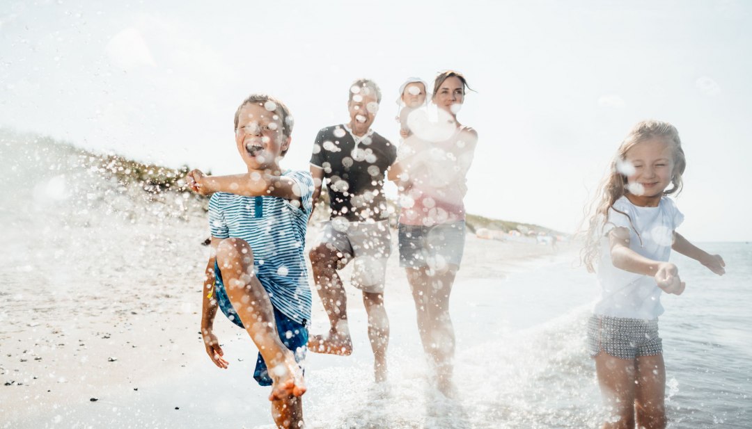 Children and parents splash around happily in the shallow Baltic Sea water on the beach at the Baltic seaside resort of Dierhagen.