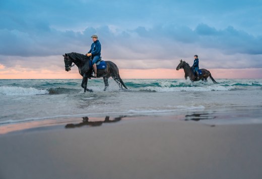 Dwóch jeźdźców na koniach jeździ po plaży o zachodzie słońca nad Morzem Bałtyckim na półwyspie Fischland-Darß-Zingst
