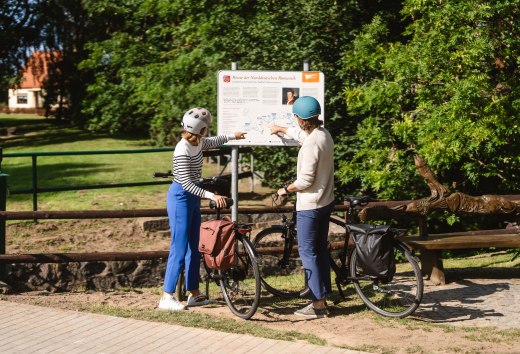 Two cyclists stand at the sign for the Route of North German Romanticism